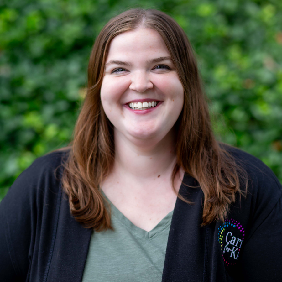 Woman with long brown hair smiles at the camera; wears a light green shirt.