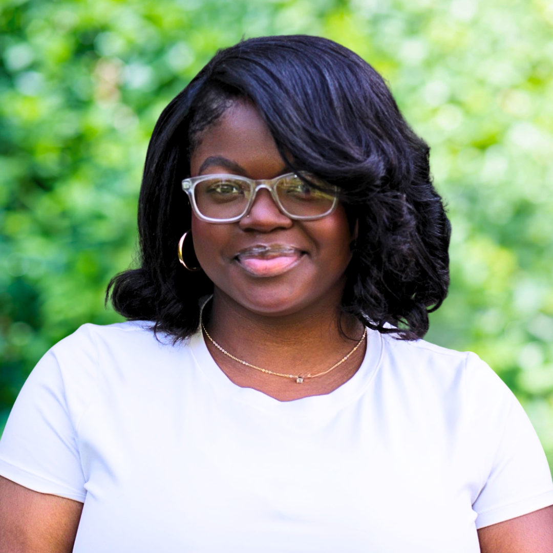 A Black woman with glasses and long dark hair smiles in a purple shirt.
