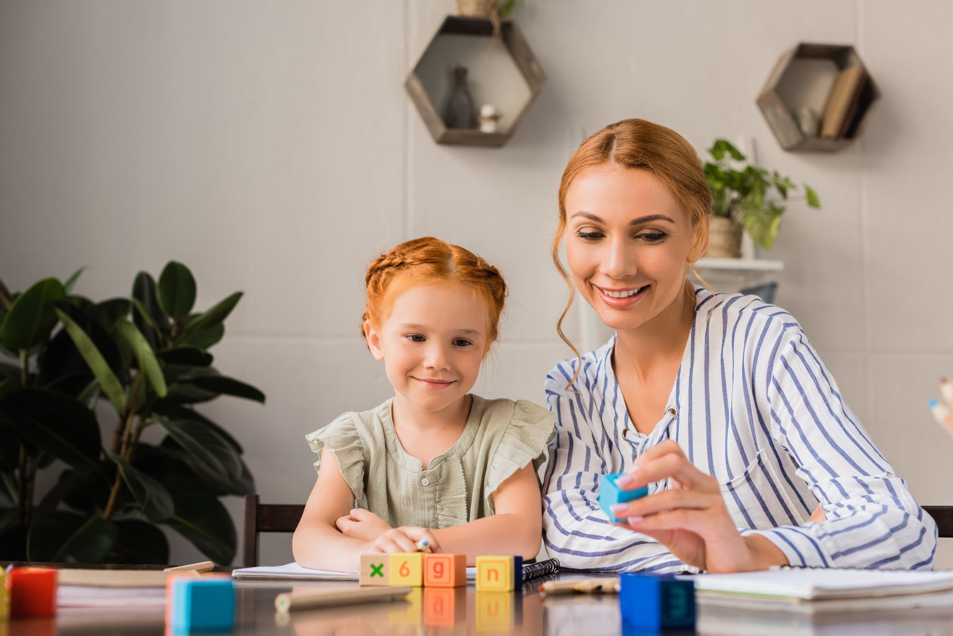 Woman and child with red hair playing with alphabet blocks at a table.