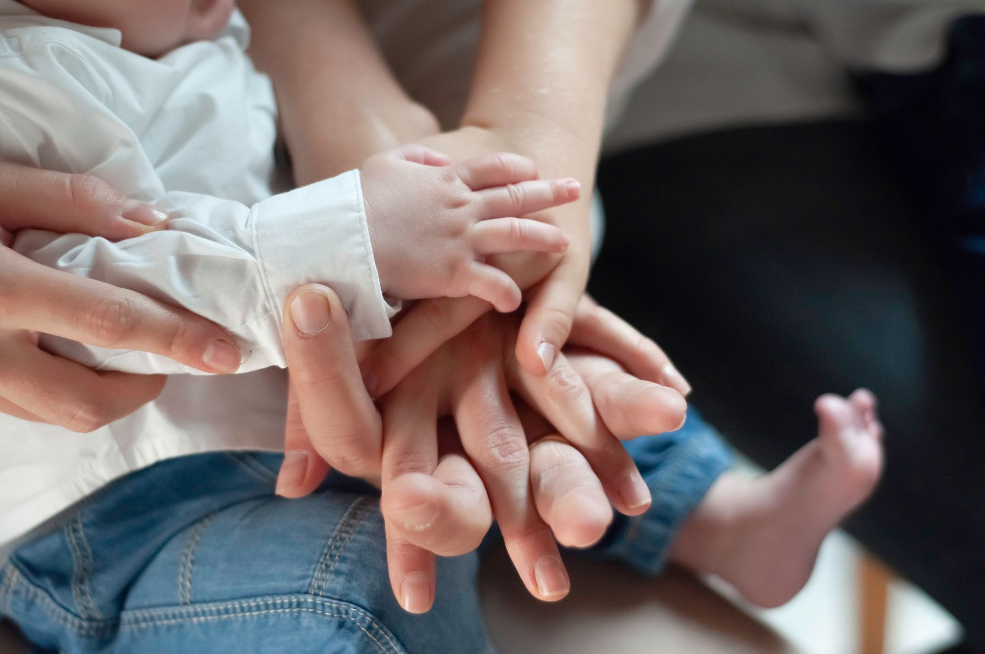 Hands of an adult and a baby, overlapping in a supportive gesture. Baby wears white shirt and jeans.