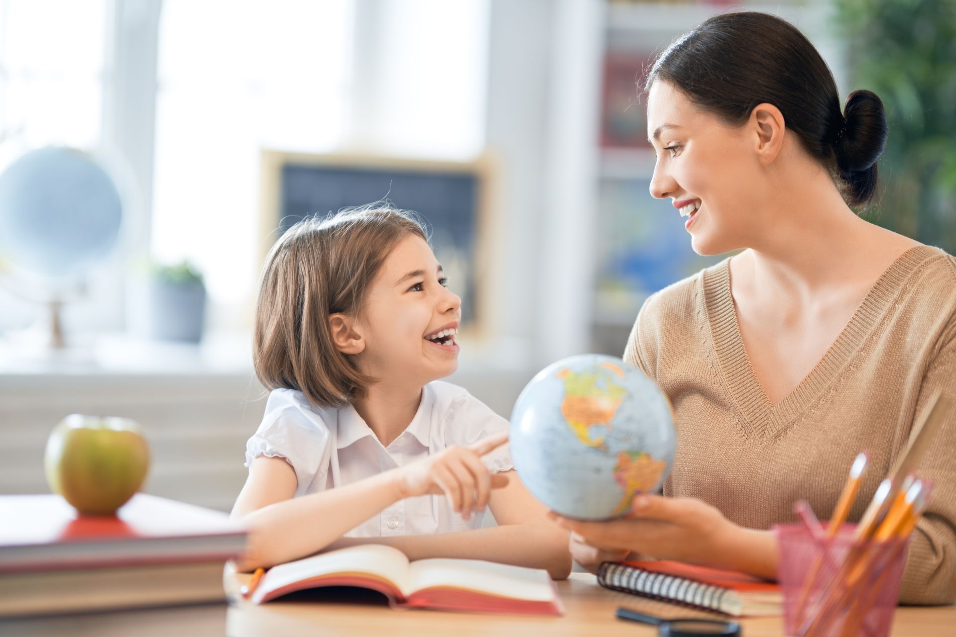 Woman and child looking at globe, smiling, and studying at a desk.