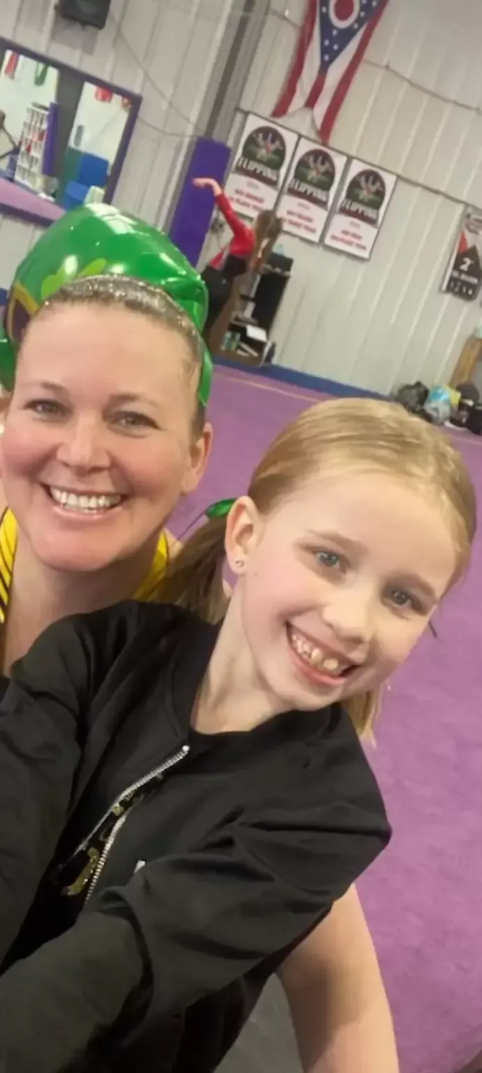A woman and girl smiling for a selfie in a gym with purple mats. Ohio flag in the background.