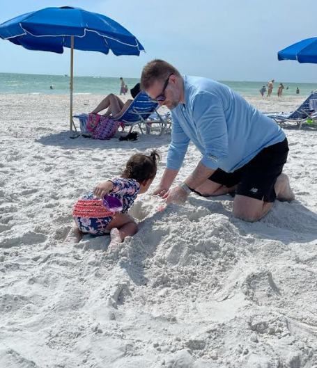 Man and child build sand castle on sunny beach under blue umbrellas.
