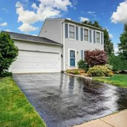 Two-story gray house with blue shutters and a wet driveway on a sunny day.