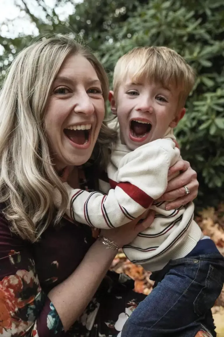 Woman holding and laughing with a child who is also laughing, outdoors.