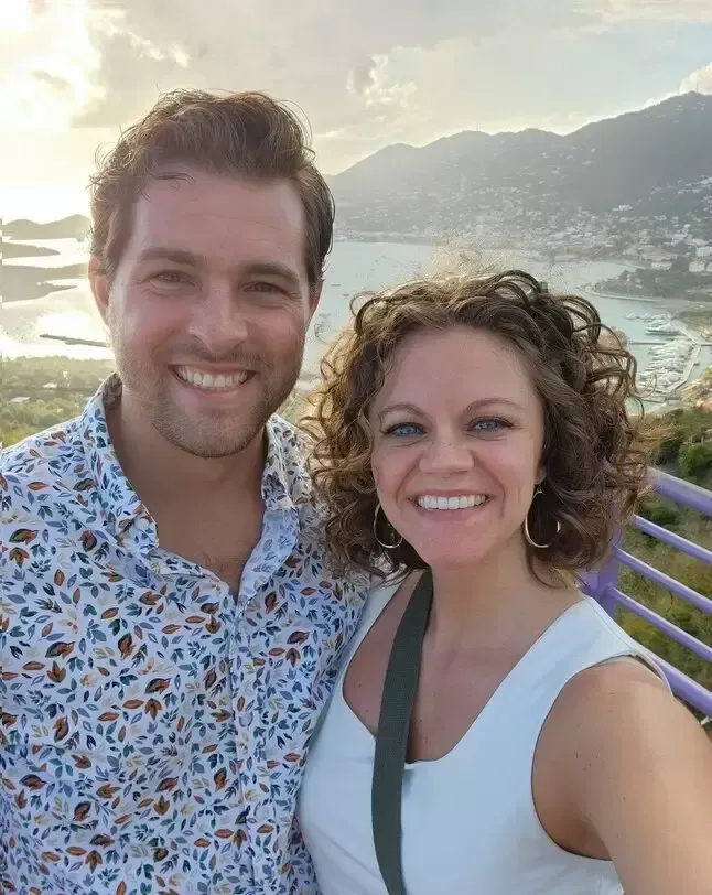 Smiling couple poses outdoors with ocean view and hazy sunset.