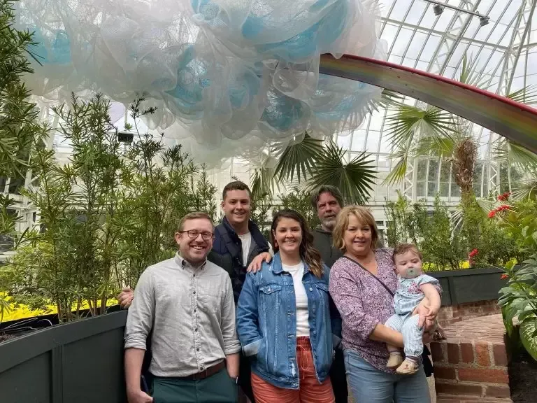Group of six people posing under a cloud sculpture with a rainbow; inside a greenhouse.