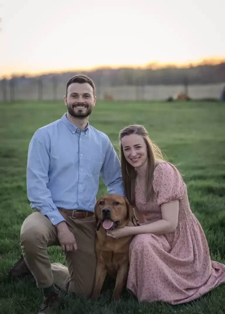 Couple kneeling with a dog in a field at sunset.
