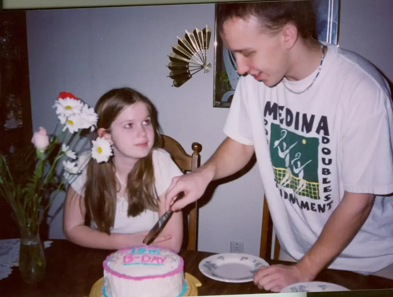 Man cutting cake for a girl with flowers in her hair at a table. Birthday celebration.