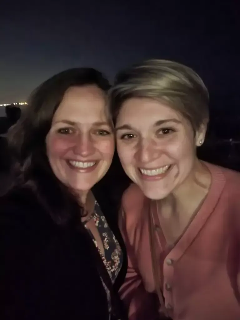 Two smiling women taking a selfie at night; one with brown hair, one with short blonde hair.