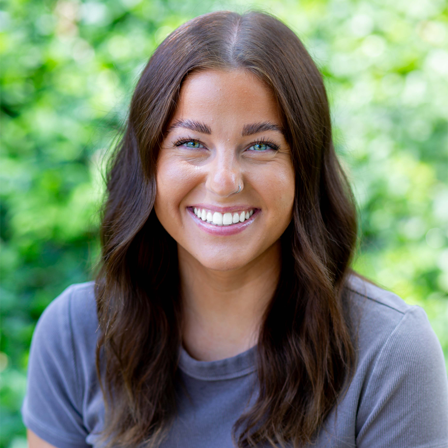 Woman with brown hair smiles, wearing a cream sweater with red and tan patterns, gold necklace.