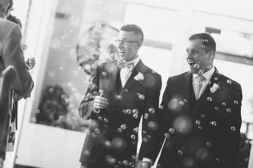 Two grooms, smiling, walking through bubbles after their wedding ceremony.