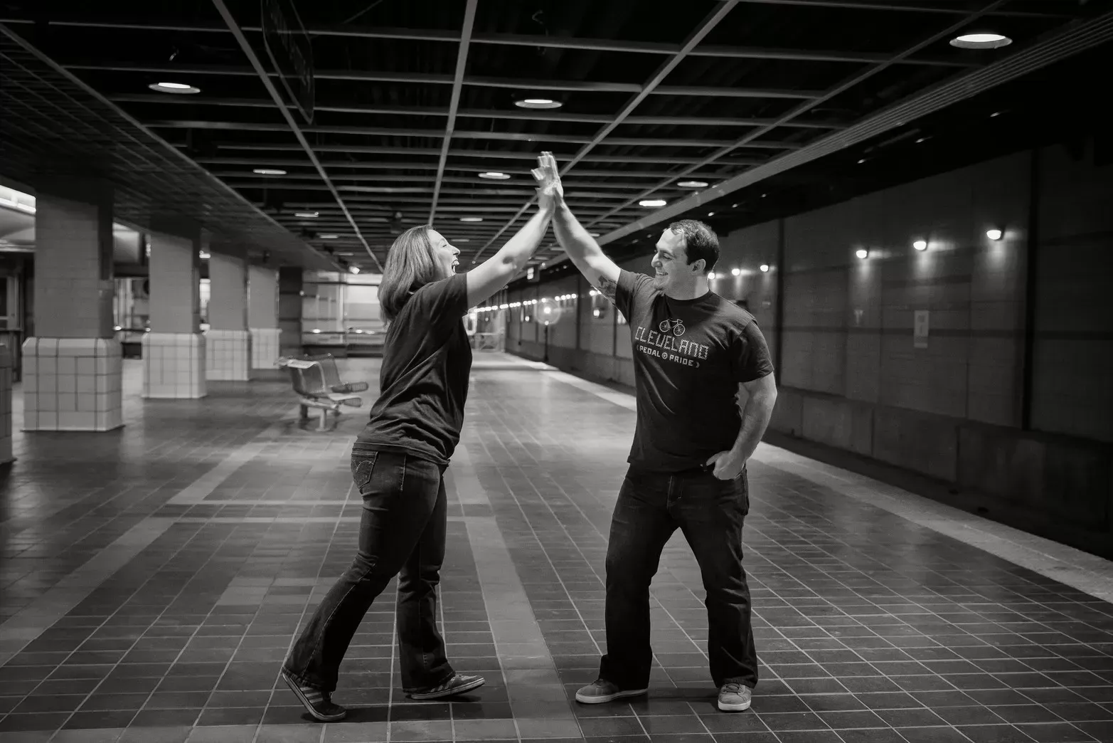 Two people high-fiving in a subway station. Black and white photo.