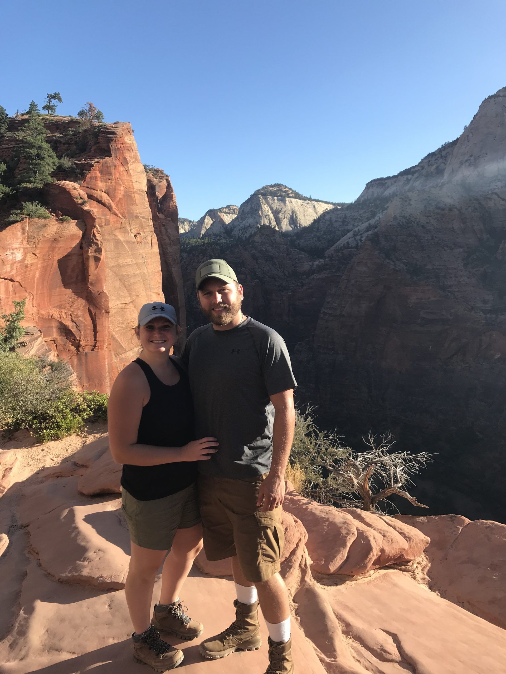 Couple poses on a red rock mountain overlooking a canyon. Clear blue sky.