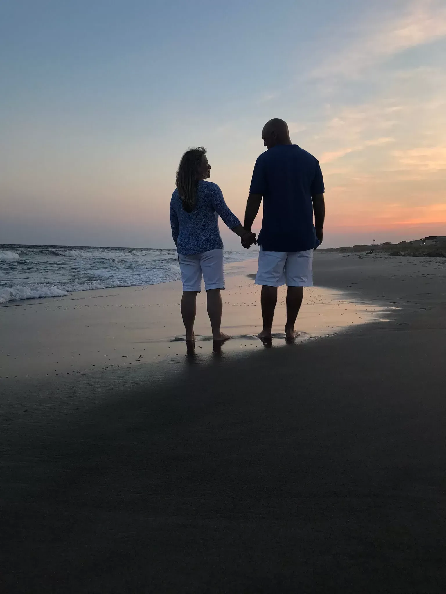 Couple walking hand-in-hand on a beach at sunset.