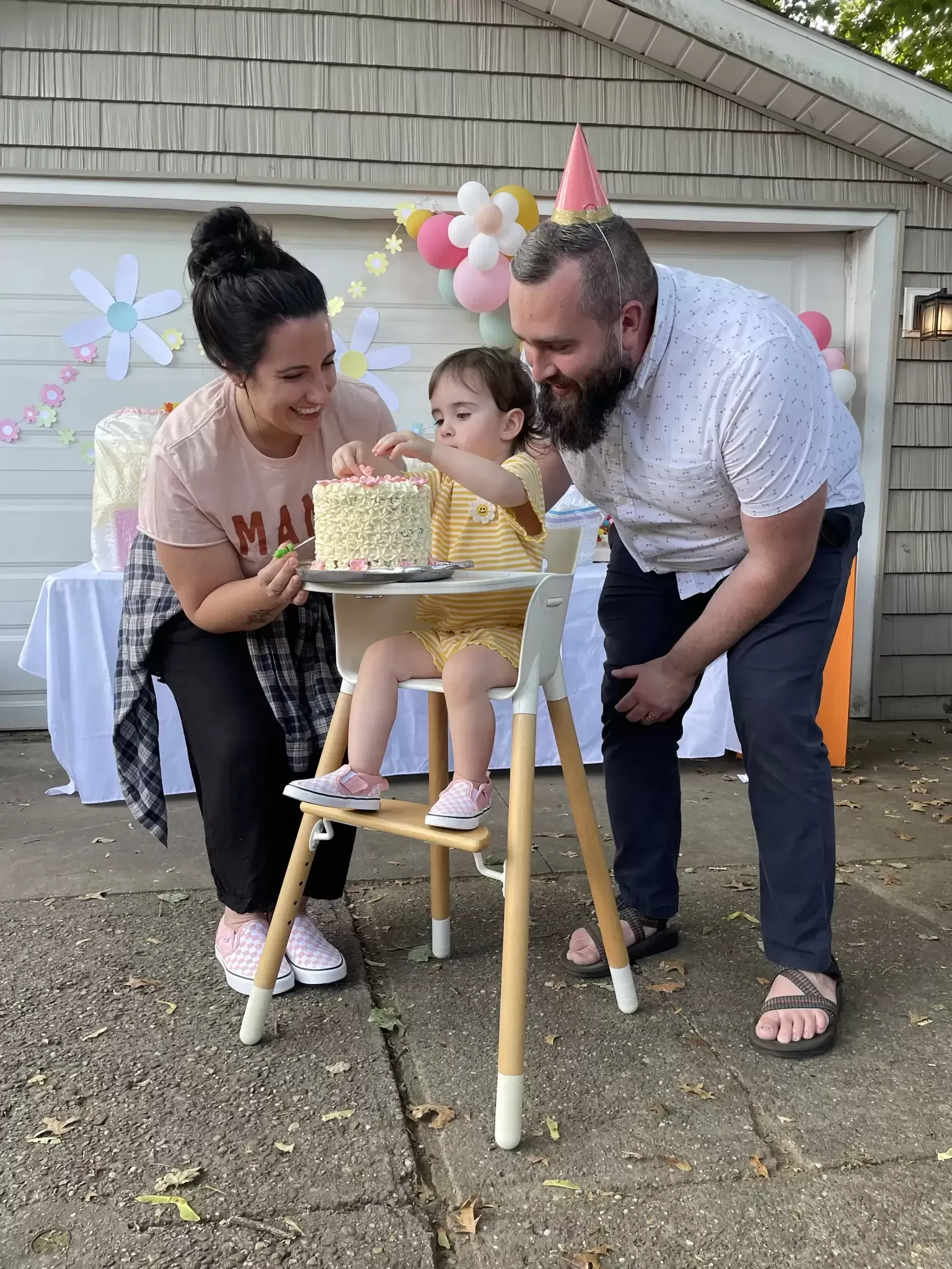Family celebrating a baby's first birthday outdoors. Parents help the child with the cake.