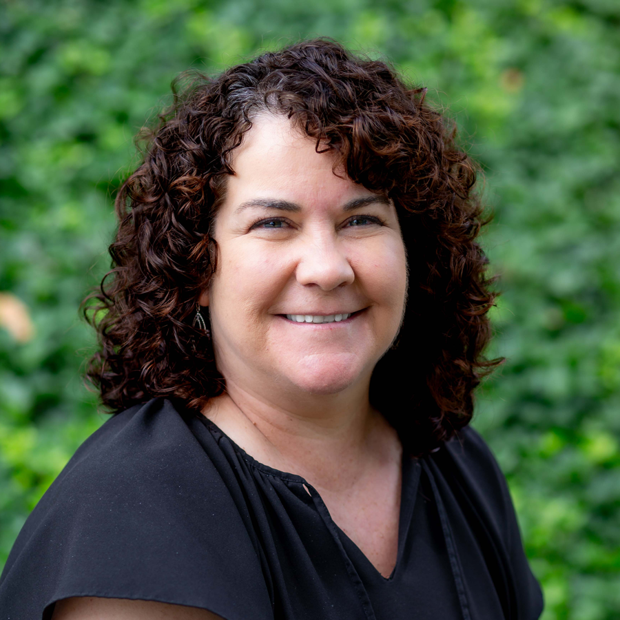 Woman with curly brown hair wearing a red cardigan and black top, smiling.