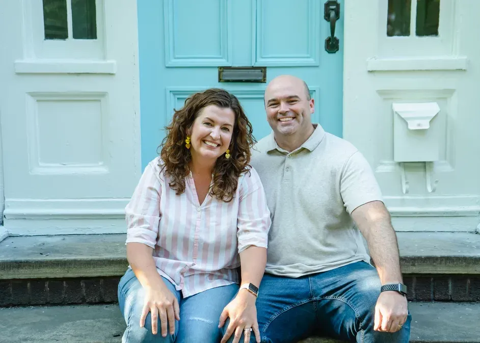 Couple smiling, sitting on porch steps in front of a turquoise door.