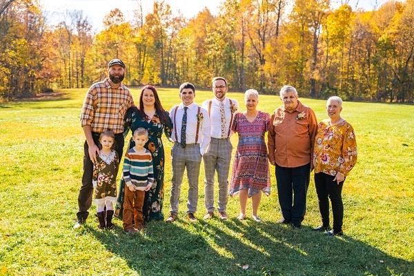 Family of nine poses in a sunlit field of golden autumn trees.