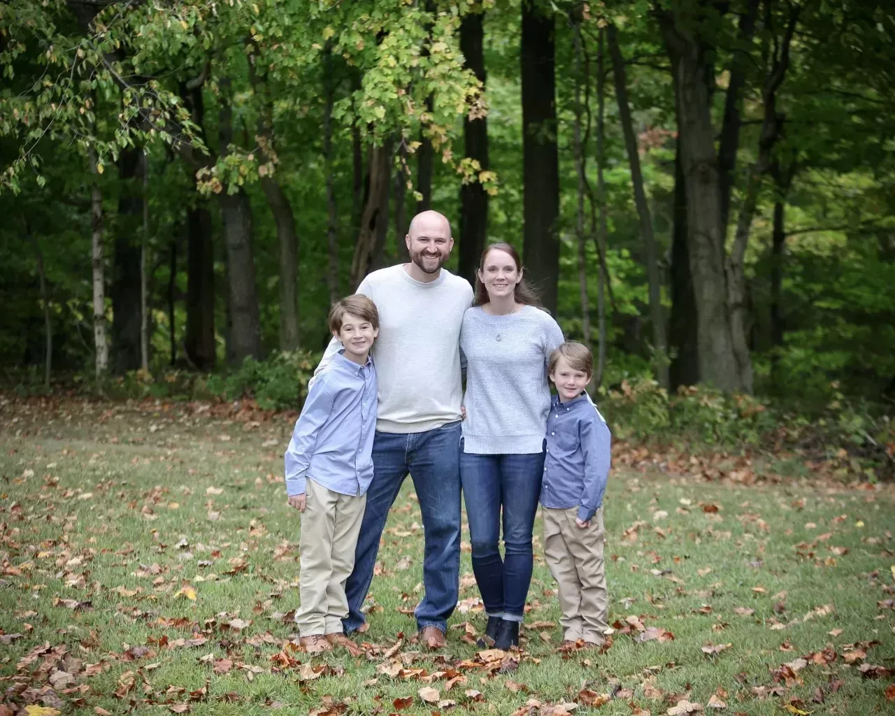 Family of four standing in a grassy area in front of trees.