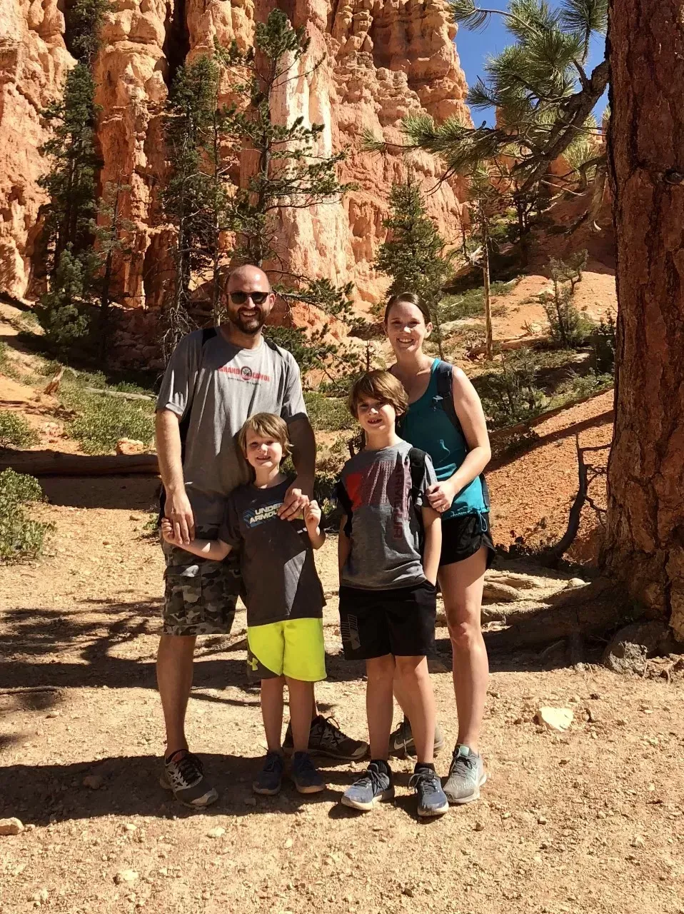 Family poses outdoors in front of red rock formations, smiling at the camera.