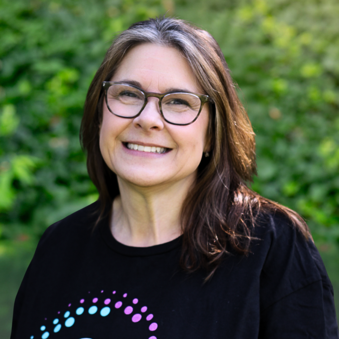 Woman with glasses smiles broadly, wearing a red cardigan over a gray shirt.