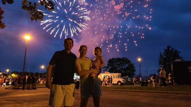 Family watching fireworks at night. Father, mother, and child smiling under colorful explosions.