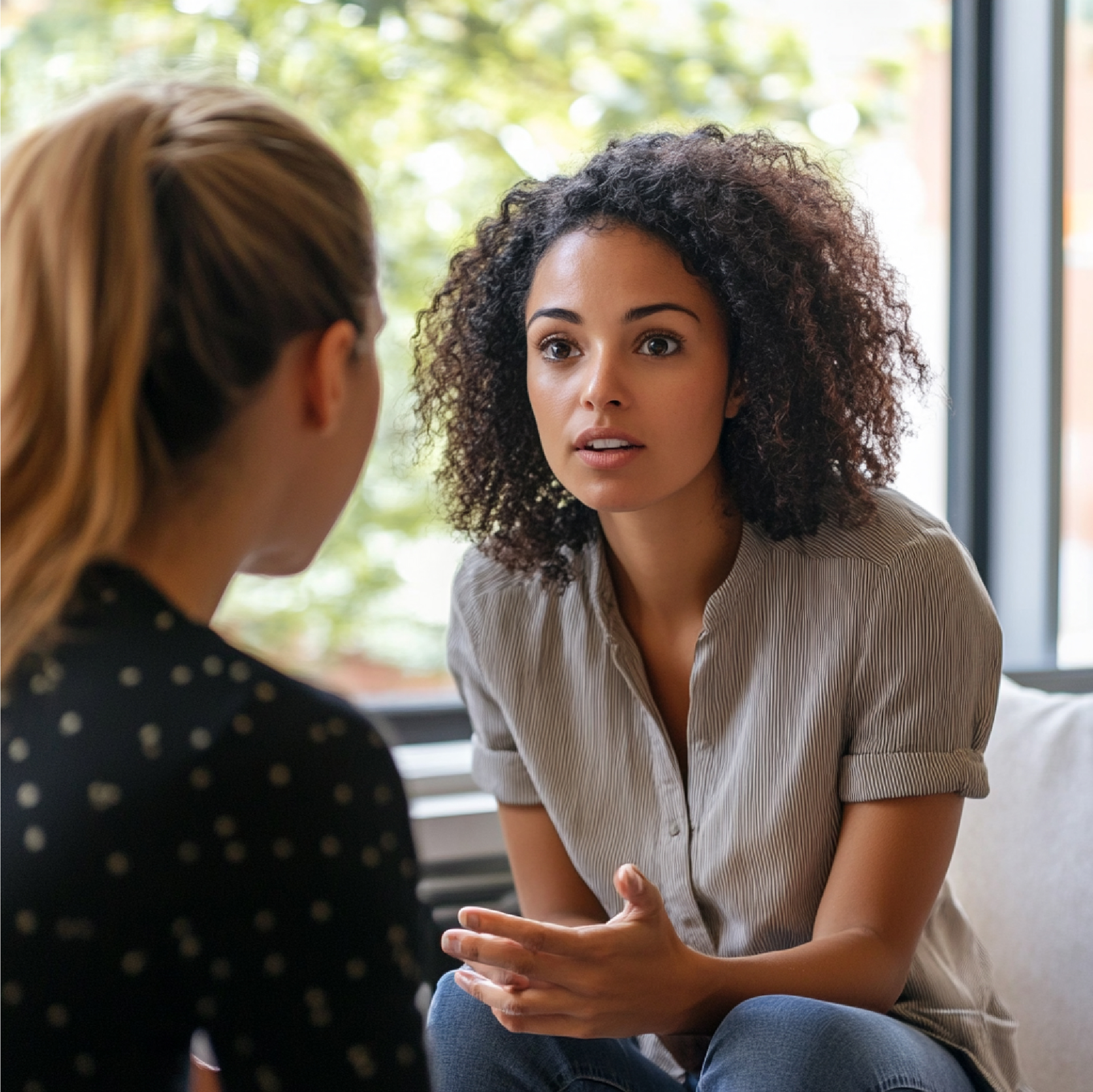 Woman with curly hair talking to another woman in an office setting.