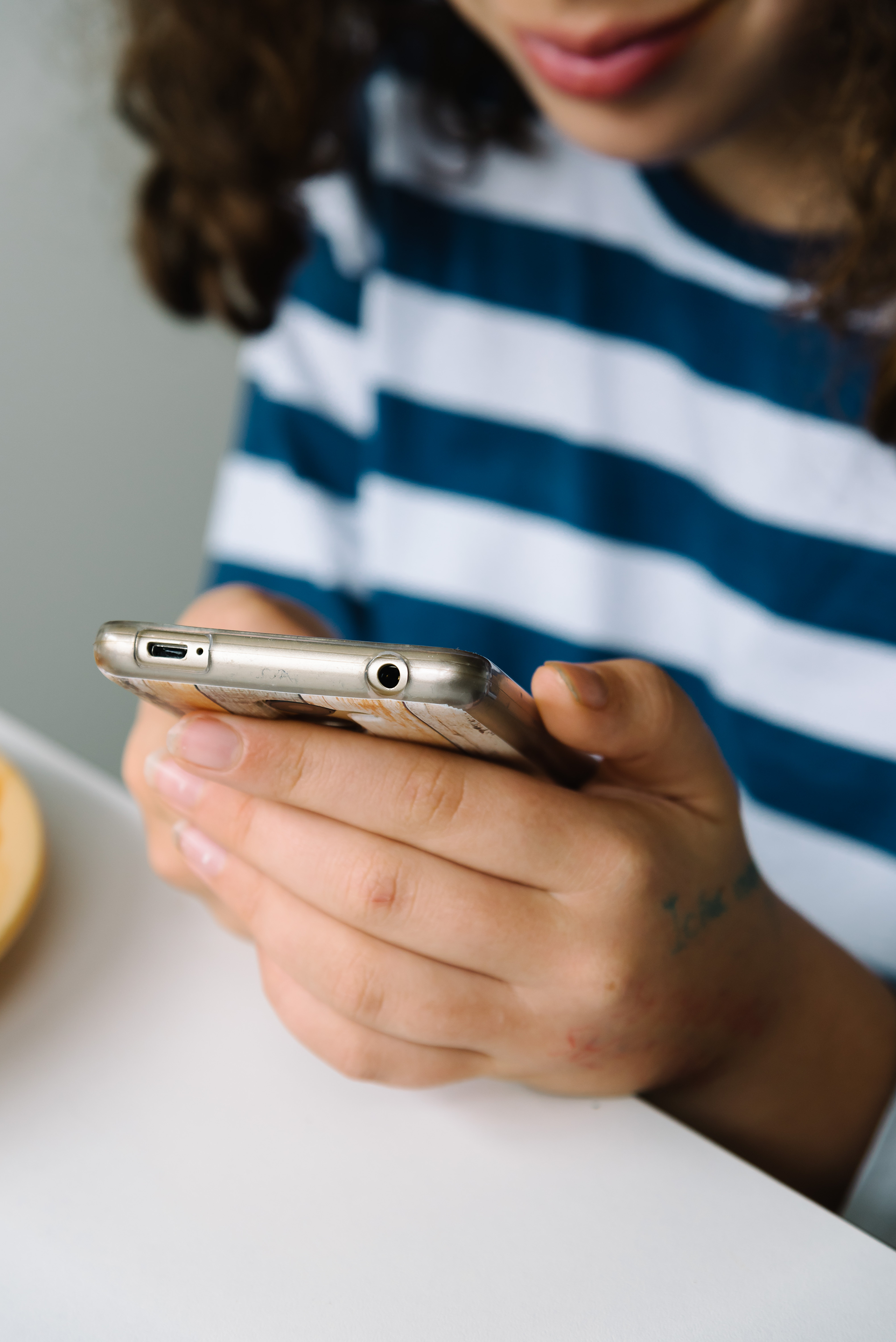 Person with curly hair in blue-striped shirt using a smartphone.