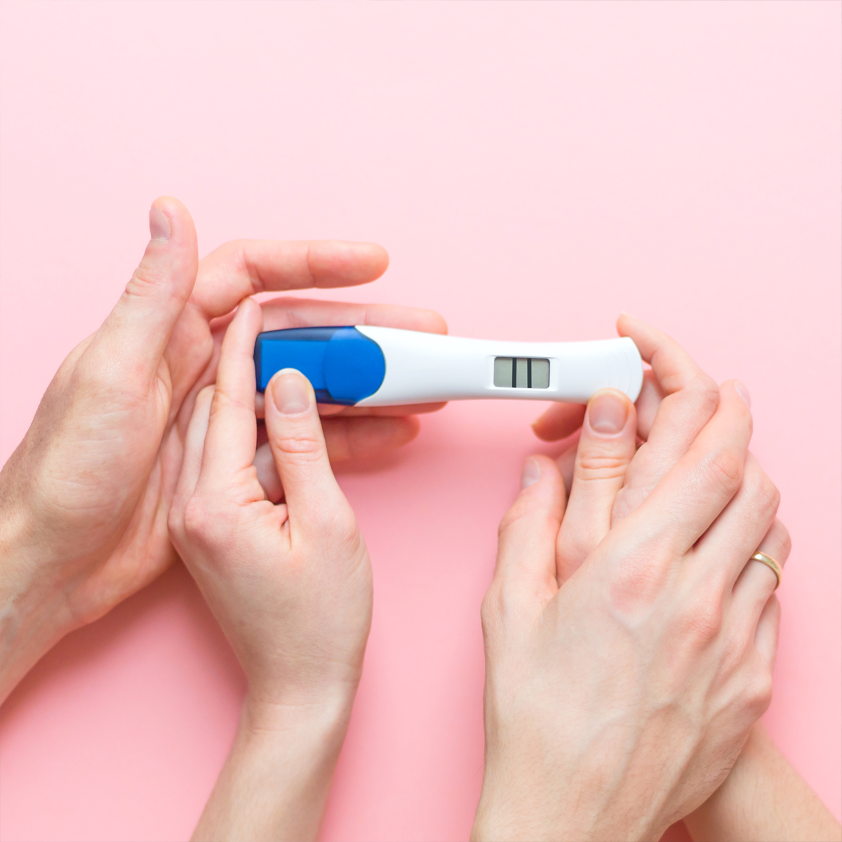 Hands holding a positive pregnancy test against a pink background.
