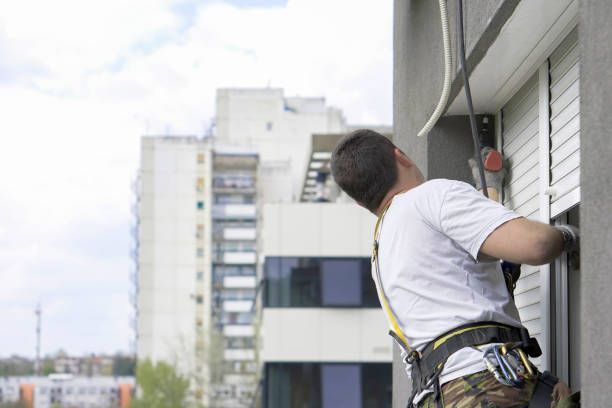 White horizontal venetian blinds partially raised to allow two cats to sit on a windowsill.
