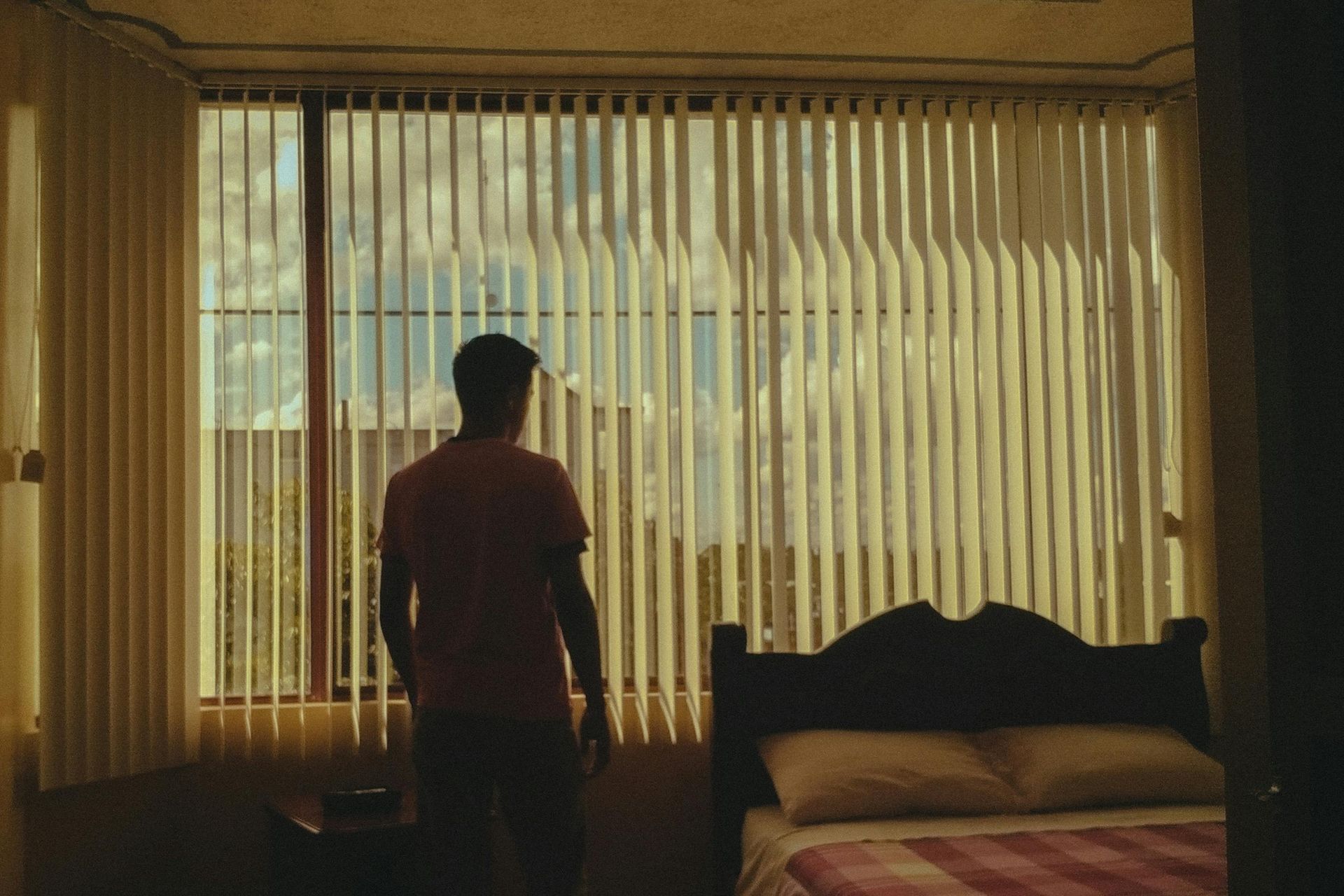 Cream vertical window blinds partially open to reveal a city view from a residential bedroom.