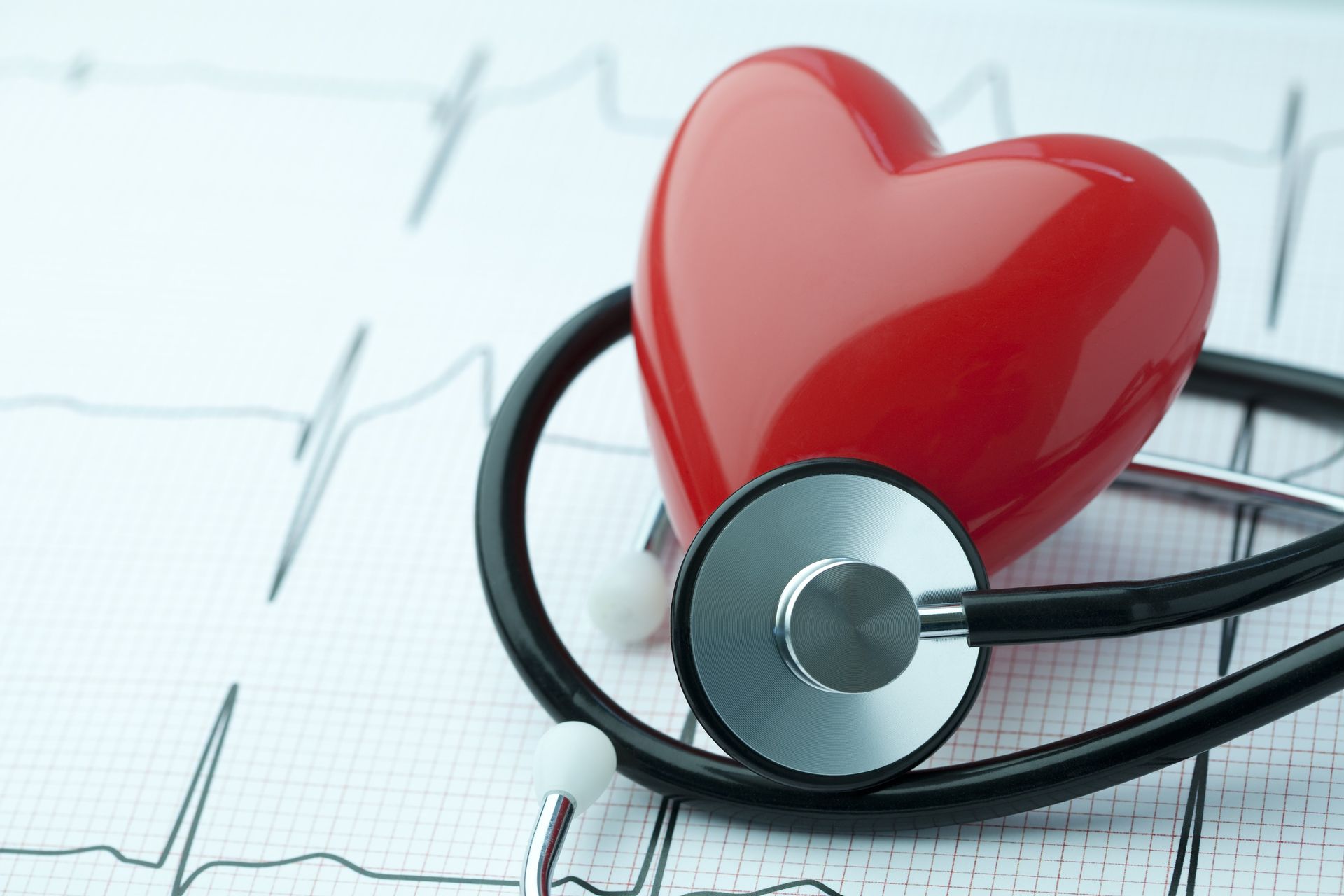 a red heart is sitting on top of a stethoscope on a heartbeat graph .