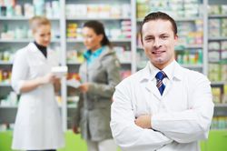 a pharmacist is standing in a pharmacy with his arms crossed .