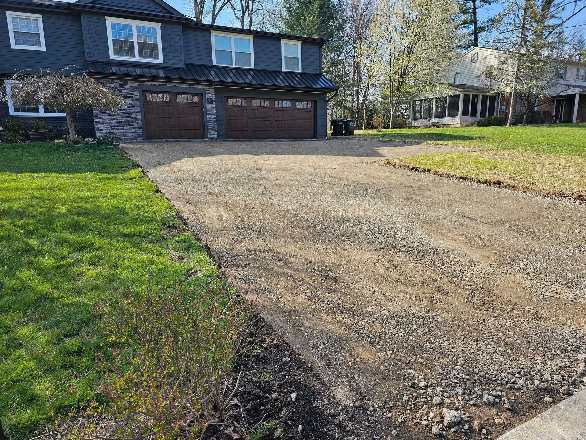 Gravel driveway leading to a two-story house with a gray exterior and a green lawn.