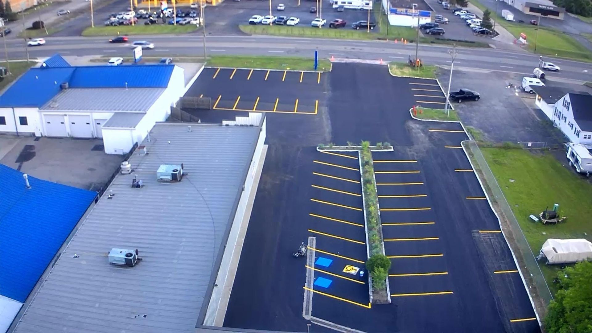 Aerial view of a parking lot with yellow parking lines, buildings with blue roofs, and a few cars and trucks.