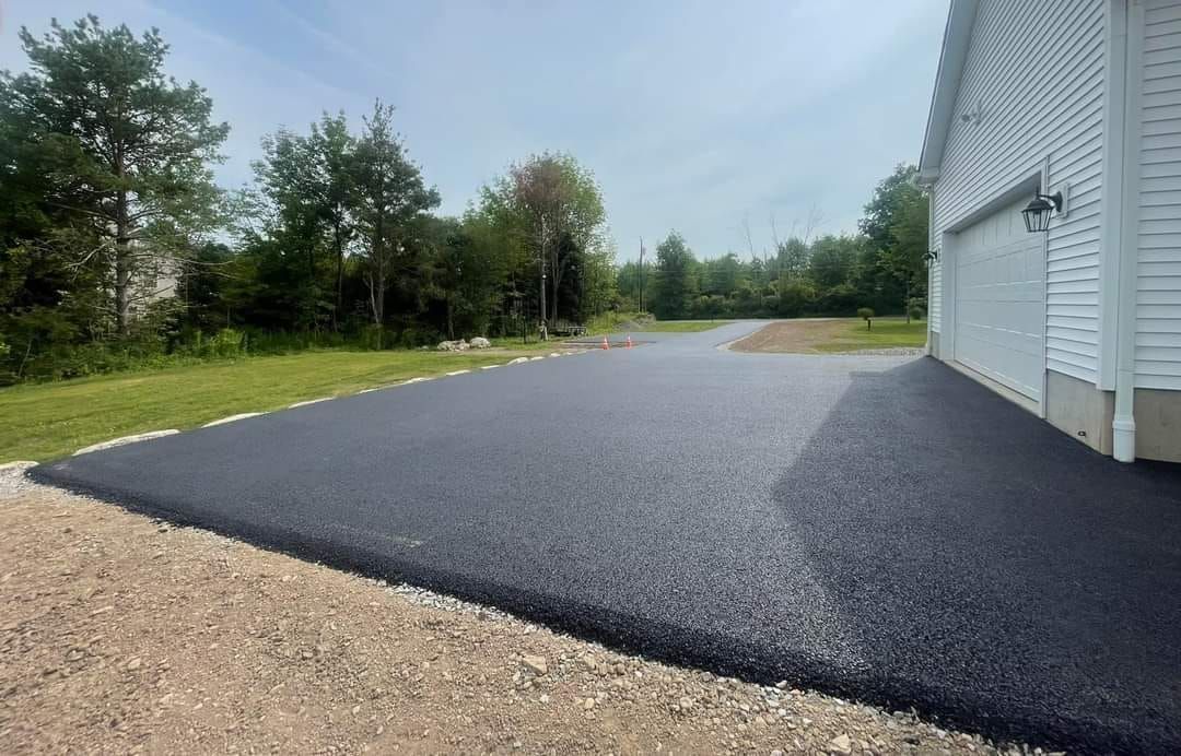 Freshly paved asphalt driveway next to a white house with a garage, sunny day.