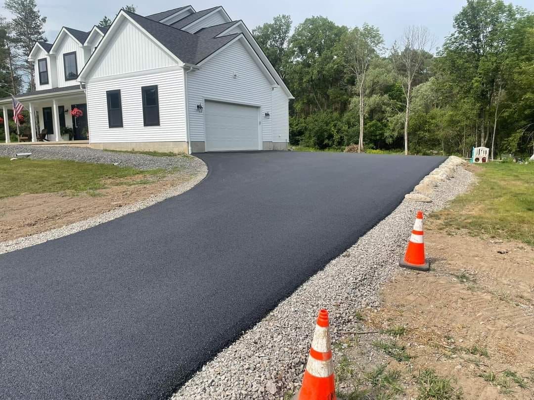 White house with a new asphalt driveway, bordered by gravel. Two orange cones are in the foreground.