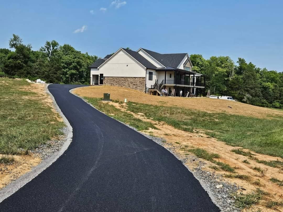 Asphalt driveway leading to a two-story house with a balcony, set on a hill.