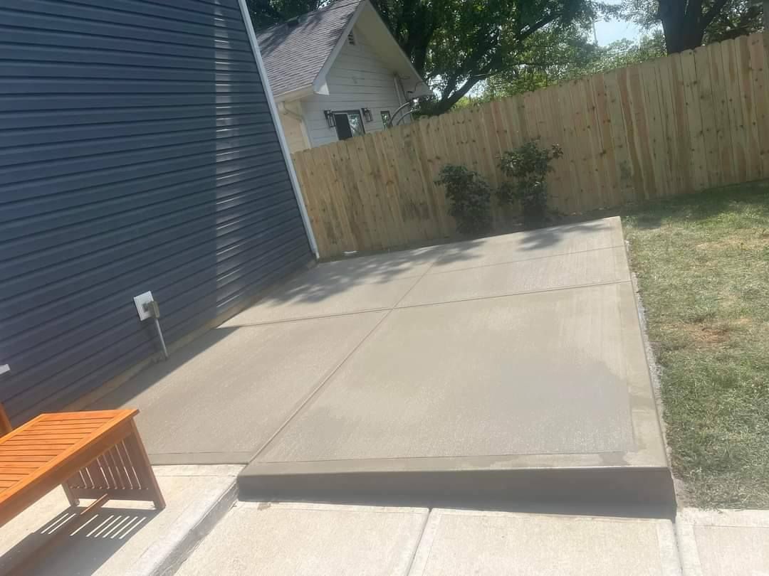 Concrete patio adjacent to a dark blue house and a wooden fence in a backyard.