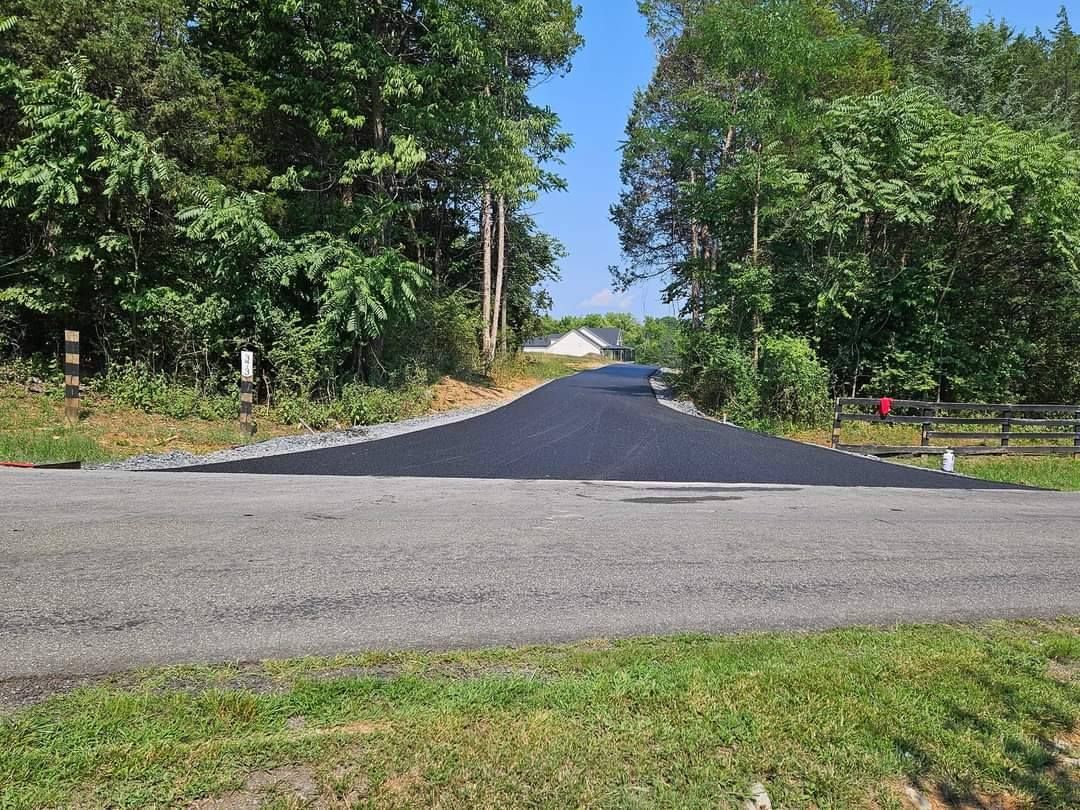 Newly paved asphalt road extending into a wooded area on a sunny day.