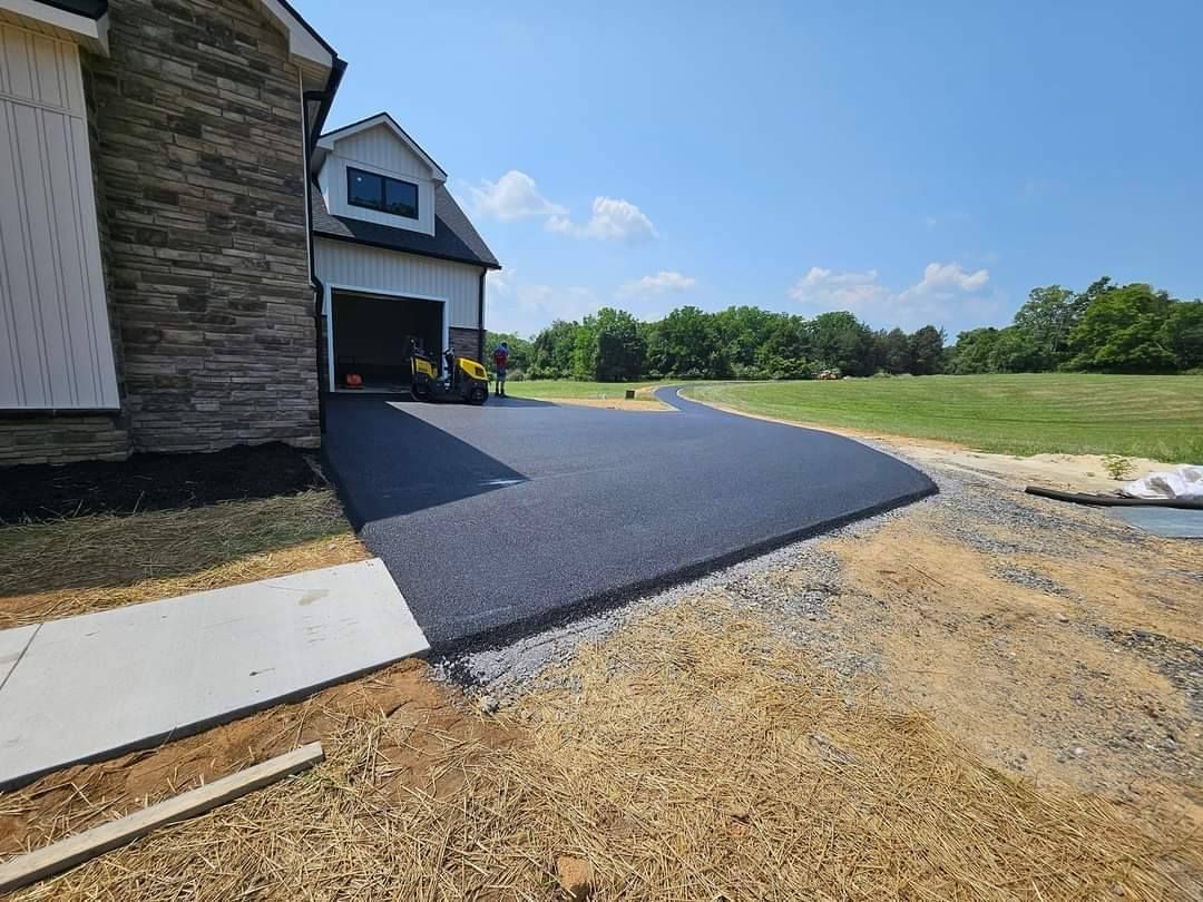 New asphalt driveway leading to a garage, alongside a house. Bright, sunny day.