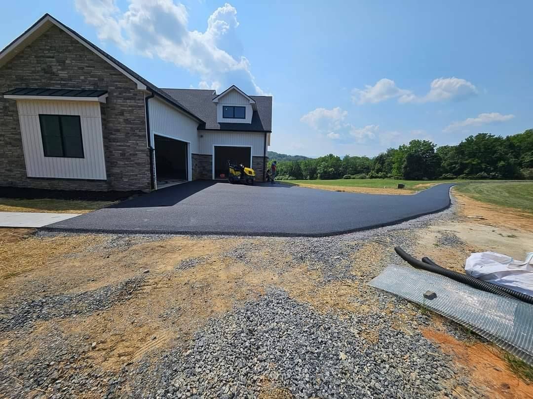 Asphalt driveway leading to a light-colored house with garage. Gravel and grass surround the new driveway.