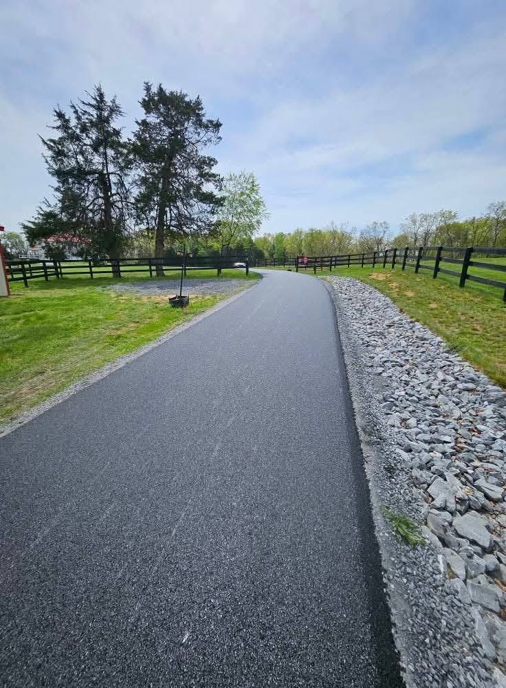 A paved road bordered by a stone wall and fence, leading toward trees and sky.