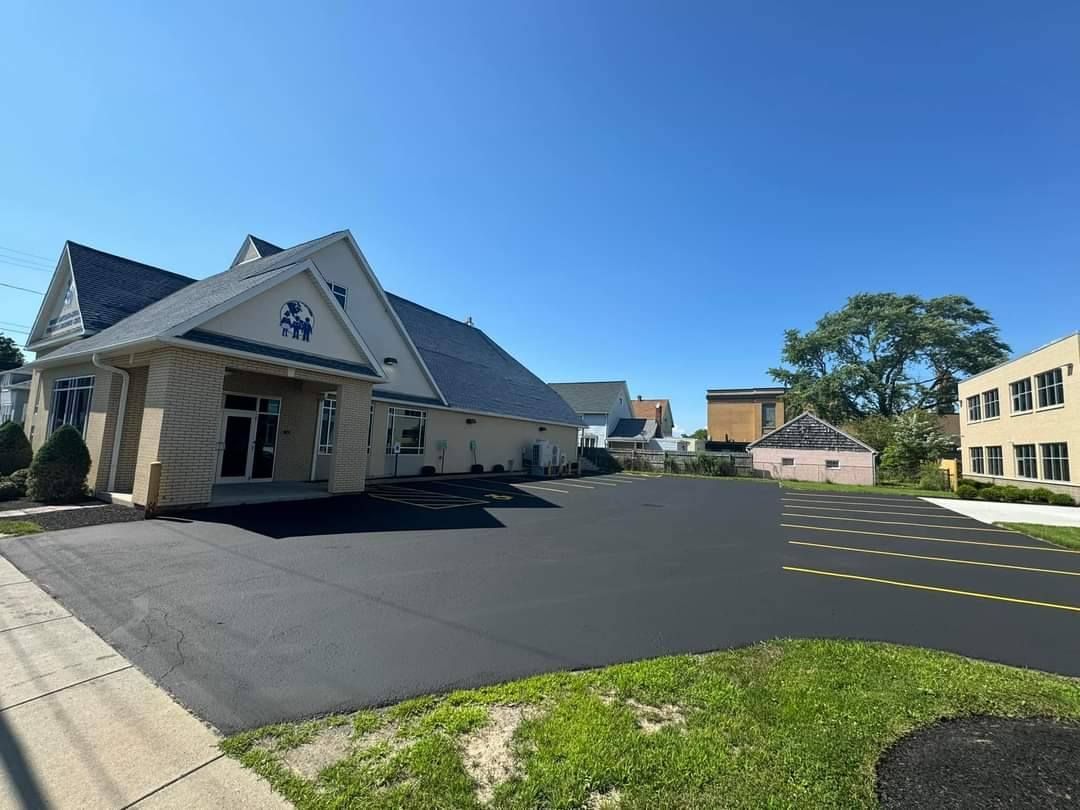 Building with dark roof and asphalt parking lot under a blue sky.