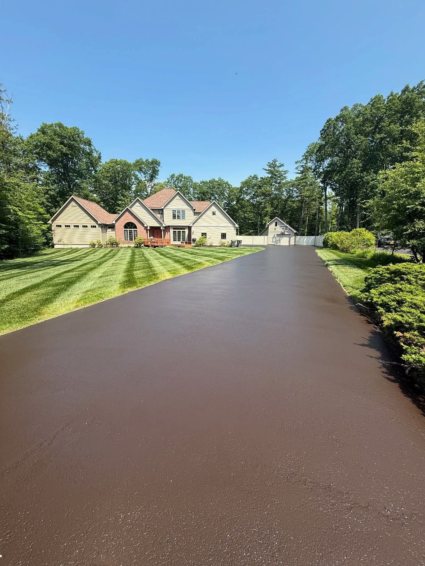 Long driveway leading to a house with a well-manicured lawn and clear blue sky.