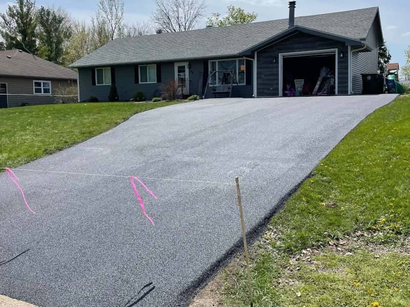 Black asphalt driveway leading up to a dark blue house with a gray roof.