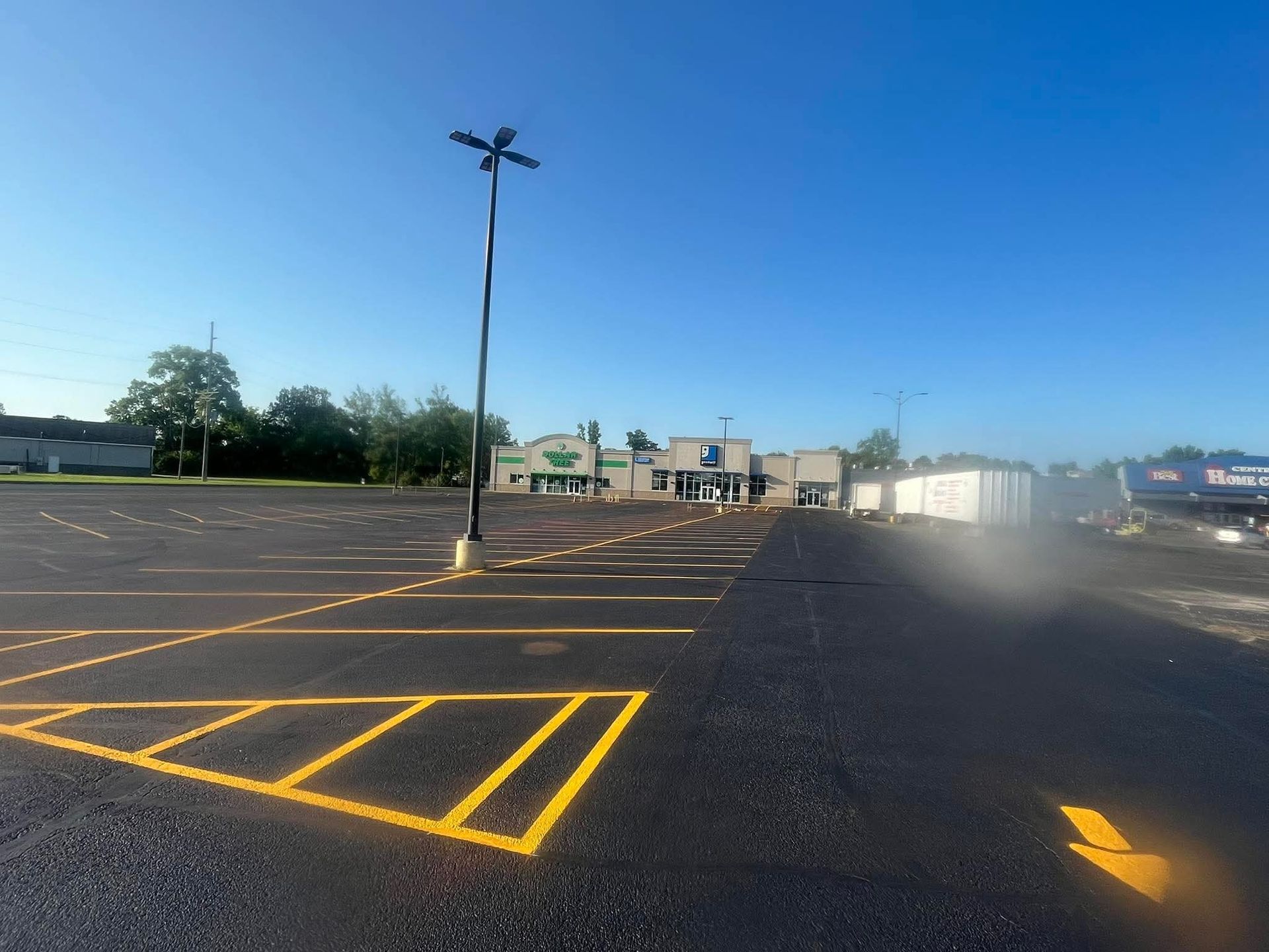 Empty parking lot with yellow lines, leading to a store with a green and blue facade on a sunny day.