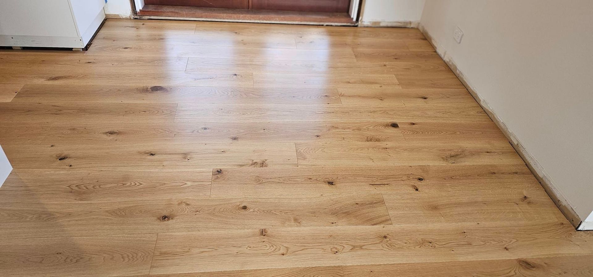 A wooden floor in a room with a door in the background.