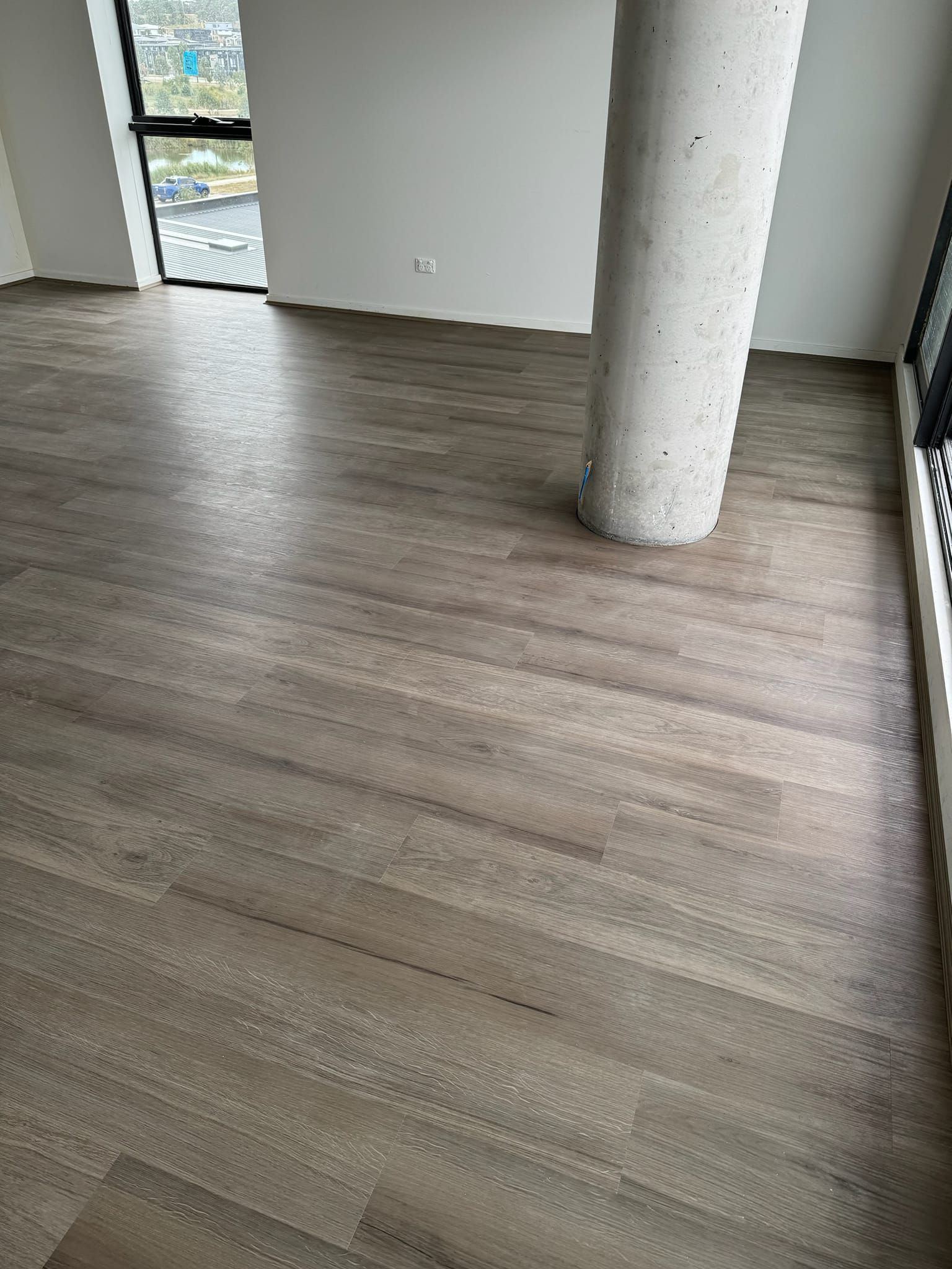 There is a pillar in the middle of the room with a wooden floor.